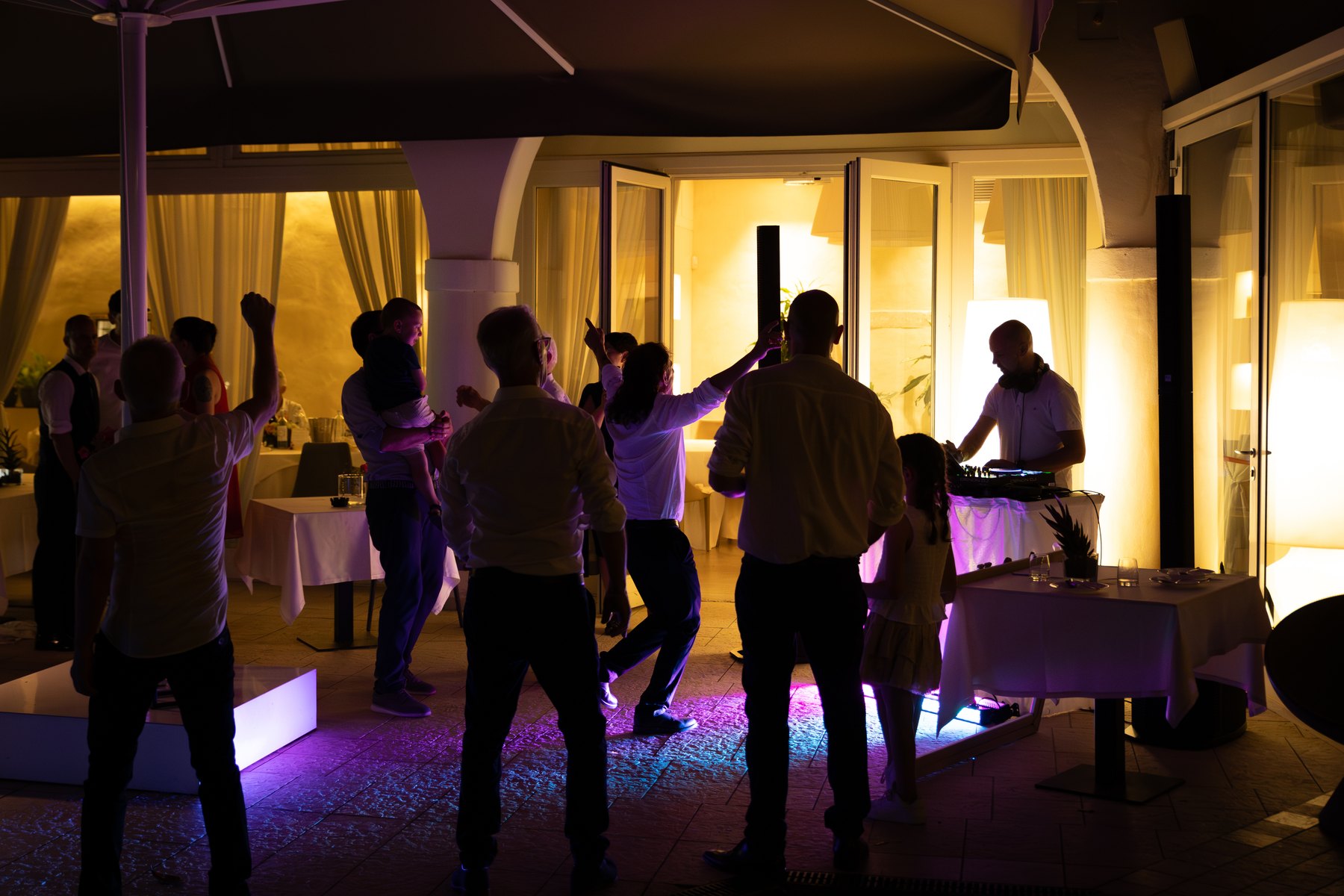 La festa di un matrimonio in sala, con persone in silhouette fra le luci.